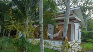 Een modern huis met een hangmat op de veranda, omringd door tropische begroeiing.