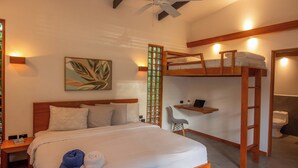 Een hotelkamer met een stapelbed, een bureau, een stoel, een bed met kussens, een plafondventilator en een kunstwerk aan de muur.