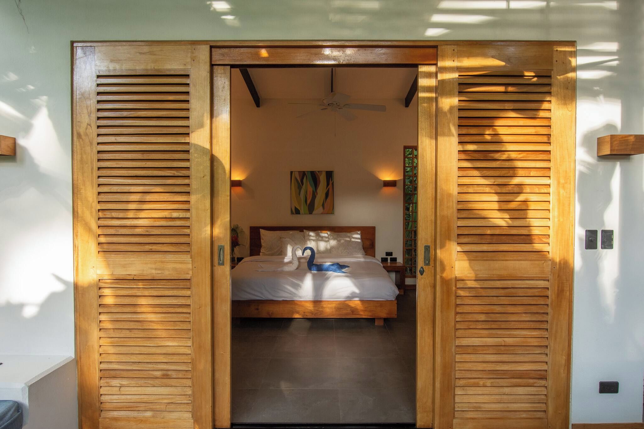 A bedroom with a bed, a ceiling fan, and a wall-mounted artwork.