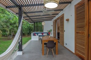A covered outdoor seating area with a table and chairs, a ceiling fan, and a view of a lush garden.