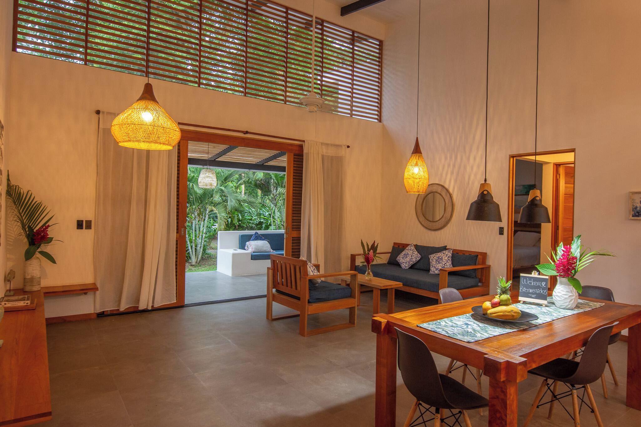 A spacious living area with a wooden dining table, two sofas, and a large window with blinds.