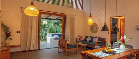 A spacious living area with a wooden dining table, two sofas, and a large window with blinds.