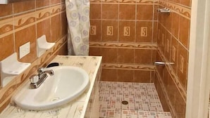 Een badkamer met een douche, wastafel, plafondventilator en betegelde vloer.