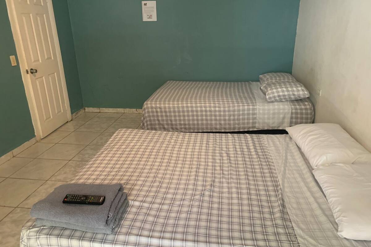 Een kamer met twee bedden, elk met een ruitdessin sprei en kussens. Een afstandsbediening ligt op een gevouwen handdoek op het bed.