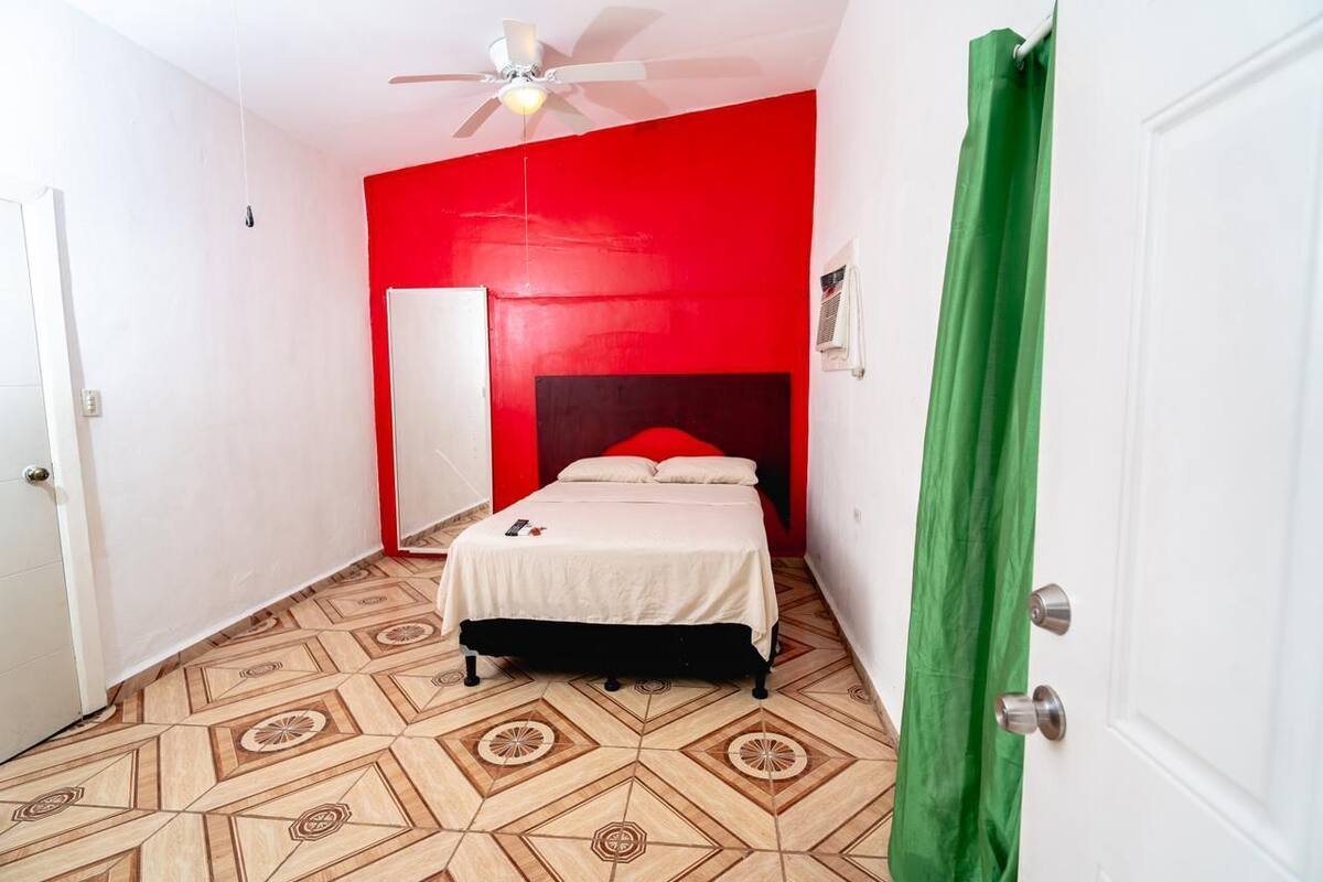 Een slaapkamer met een bed, een plafondventilator en een vloer met een geometrisch patroon.
