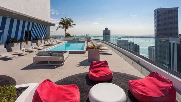A rooftop pool area with lounge chairs, a palm tree, and a view of the city skyline. - Modern Condo 2bd/2bth, Best Brickell Location (Miami)