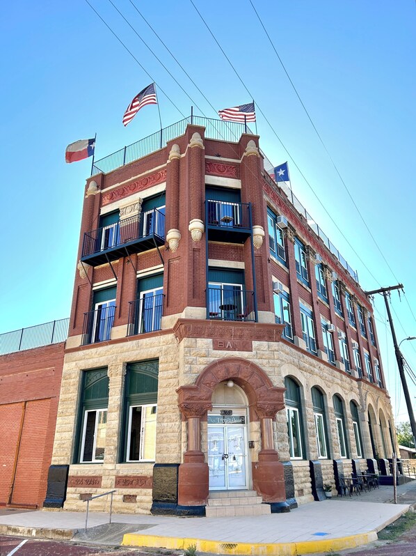 A historic building with a prominent entrance, multiple balconies, and flags on the roof. - 3E Sunrise View (Honey Grove)