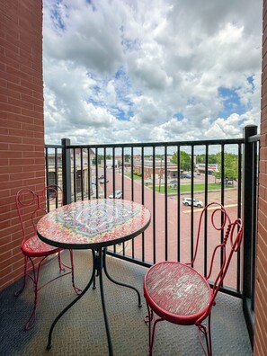 A balcony with a round table and two chairs, a view of a parking lot, and a cloudy sky. - 3E Sunrise View (Honey Grove)