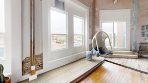 A room with large windows, a hanging chair, a small table with a vase, and a wooden floor. - 3E Sunrise View (Honey Grove)