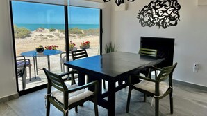 Ein Essbereich mit großem Tisch und Stühlen, einer Kandelaber, einem Kamin und Blick auf den Strand.