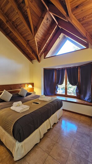 A bedroom with a large bed, a skylight, and a view of the outdoors. - POSADA DEL CIPRES (Villa La Angostura)
