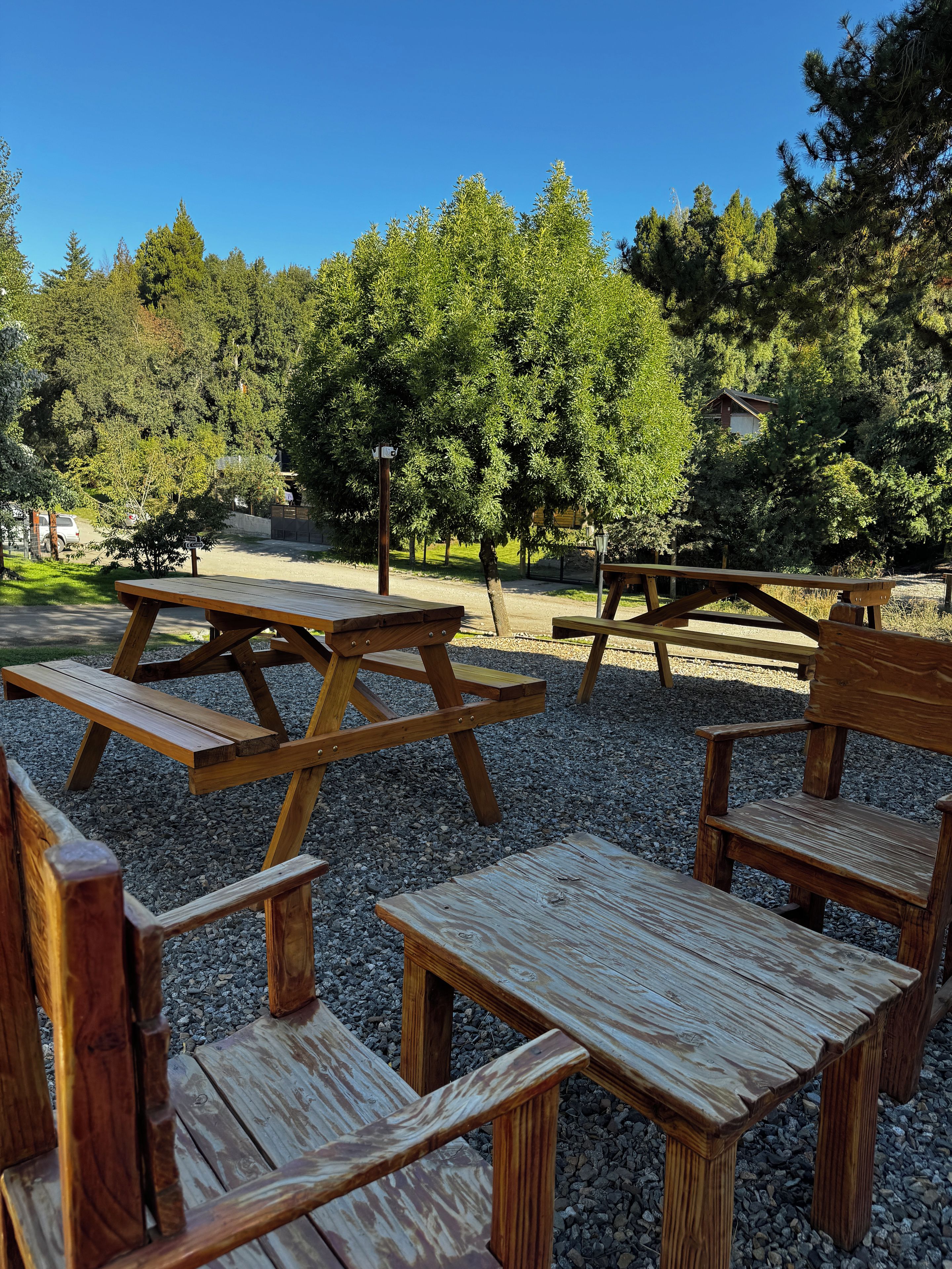 Un'area picnic con panche e tavoli di legno, circondata da ghiaia e alberi.