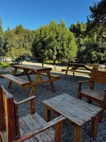 Un área de picnic con bancos y mesas de madera, rodeada de grava y árboles.
