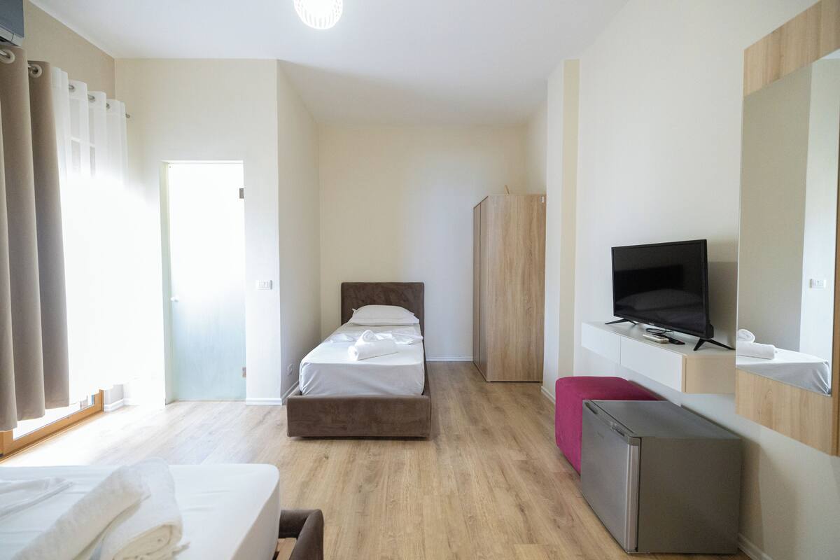 A modern hotel room with a bed, a TV, a wardrobe, and a desk.