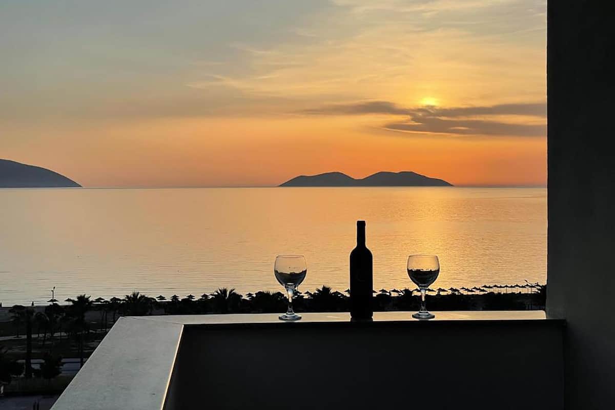 A balcony with a view of the sea at sunset, featuring a bottle and two wine glasses.