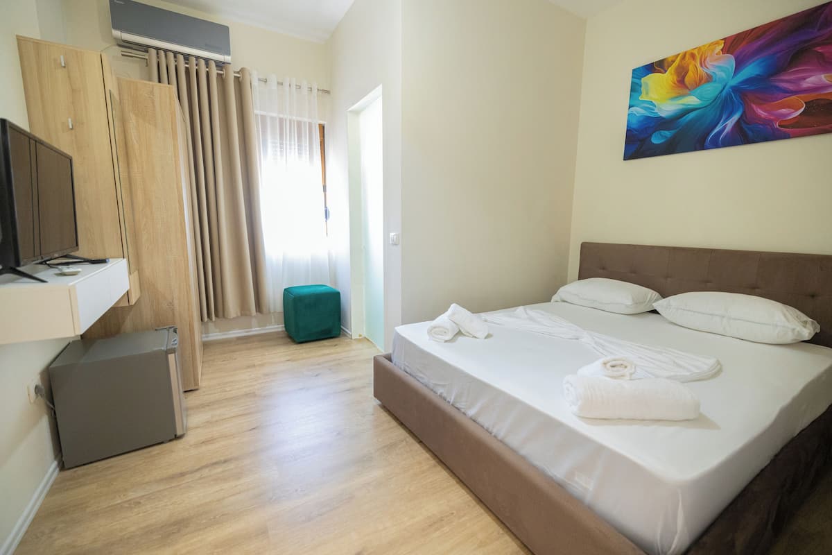 A hotel room with a bed, a TV, a desk, and a painting on the wall.
