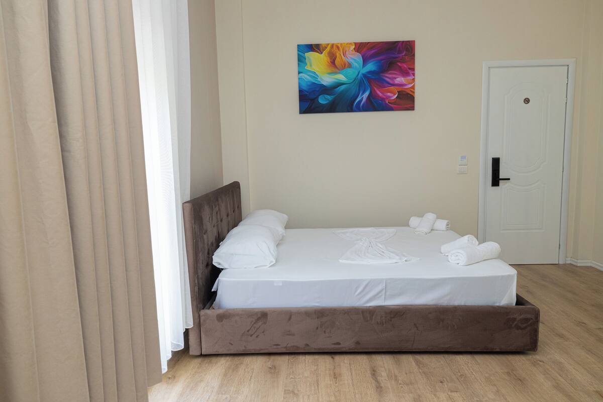 A neatly made bed with white linens, a wooden headboard, and a colorful abstract painting on the wall.
