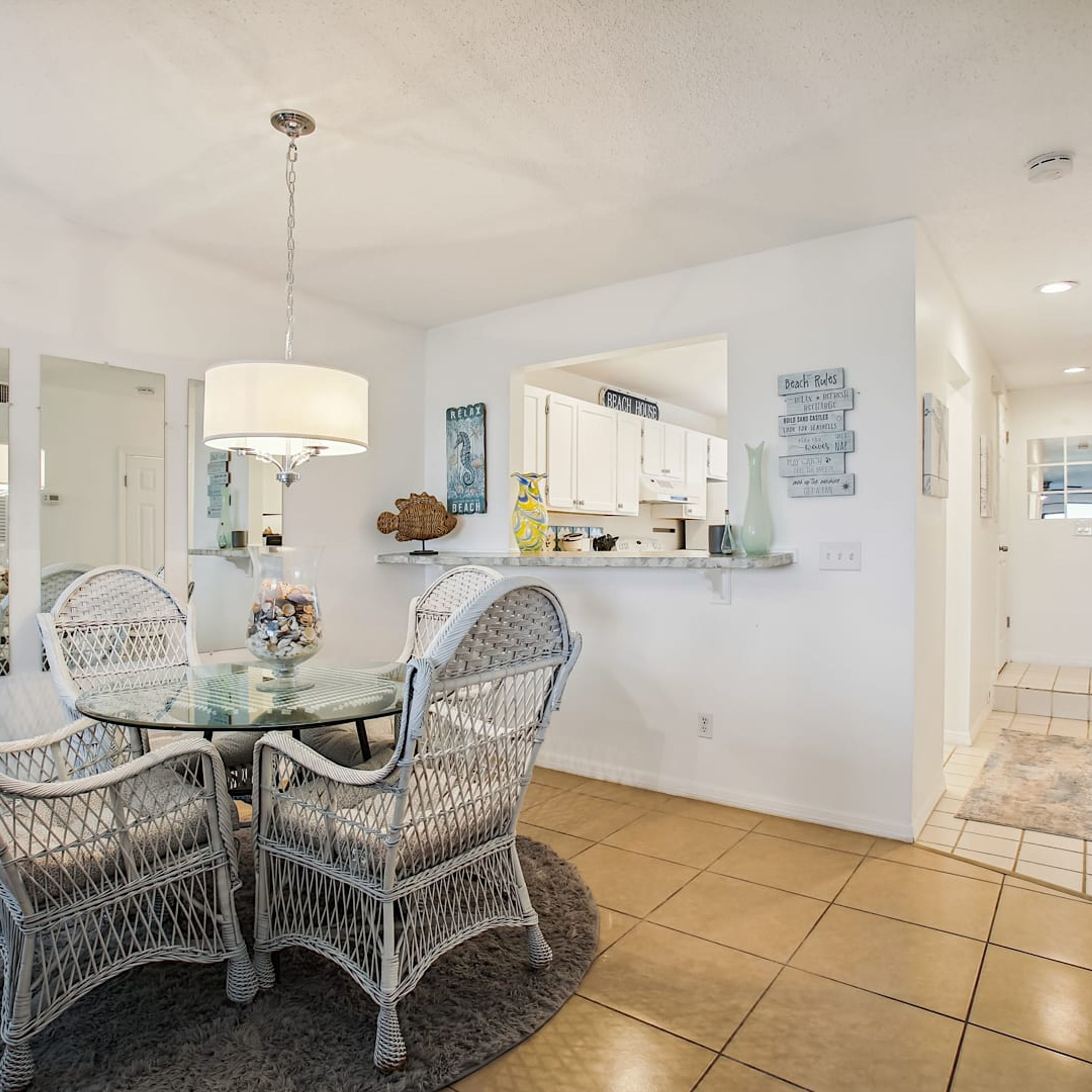A dining area with wicker chairs, a glass table, and a hanging light fixture.