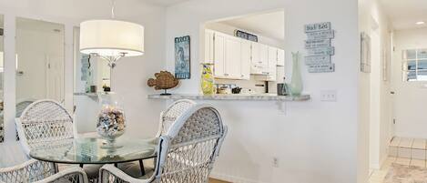 A dining area with wicker chairs, a glass table, and a hanging light fixture.