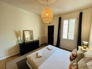 Un dormitorio con cama, cómoda, espejo, ventana y lámpara colgante.