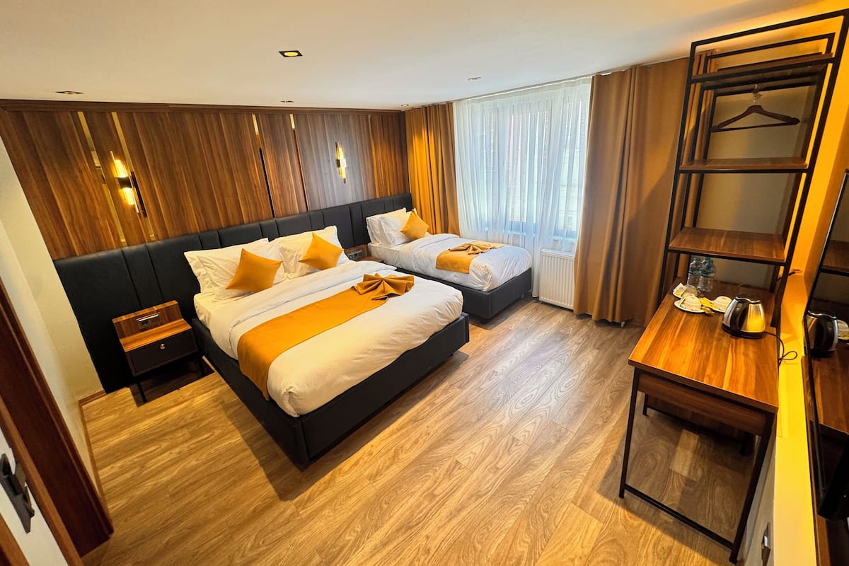 Une chambre d’hôtel avec deux lits, un plancher en bois, une petite table avec une bouilloire et une armoire avec une tringle pour suspendre les vêtements.
