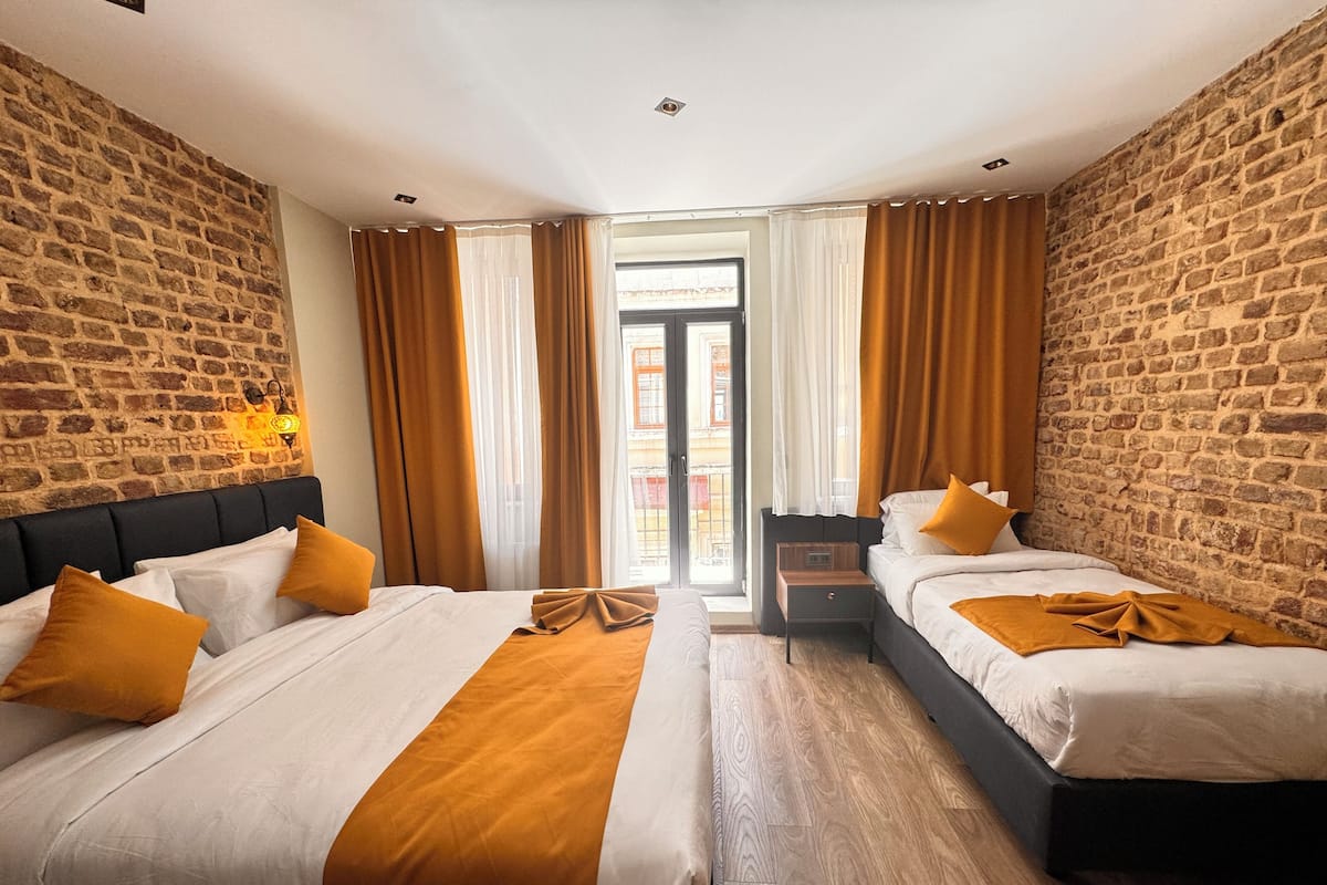Une chambre d’hôtel avec deux lits, un mur en briques, un plancher en bois et une vue sur l’extérieur, visible à travers une porte vitrée.