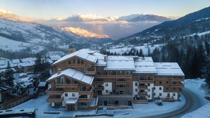 A large, multi-story lodge with a snow-covered roof, surrounded by a mountainous landscape. - Résidence l’Ecrin d’Argent by My Mountain Resort (Les Avanchers-Valmorel)