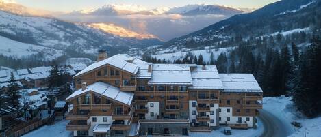 A large, multi-story lodge with a snow-covered roof, surrounded by a mountainous landscape.