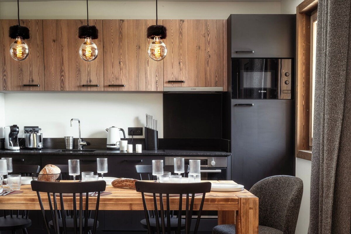 Une cuisine moderne avec des meubles en bois, un réfrigérateur noir et un coin repas comprenant une table et des chaises en bois.
