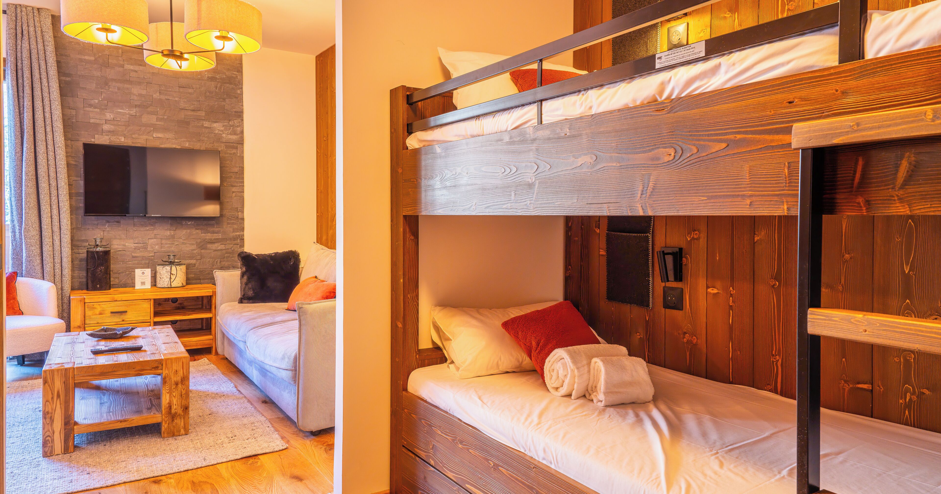 Une pièce chaleureuse avec un lit superposé en bois, un téléviseur à écran plat fixé au mur, une table basse en bois et un canapé confortable.