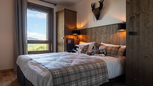 A bedroom with a large bed, wooden headboard, a mounted deer head, a window with a view, and a teddy bear on the bed. - Résidence l’Ecrin d’Argent by My Mountain Resort (Les Avanchers-Valmorel)