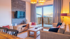 A cozy living room with a stone wall, a flat-screen TV, a wooden coffee table, and a sofa with cushions. - Résidence l’Ecrin d’Argent by My Mountain Resort (Les Avanchers-Valmorel)