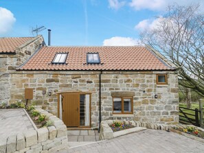 A stone building with a tiled roof, a wooden door, and a small window.