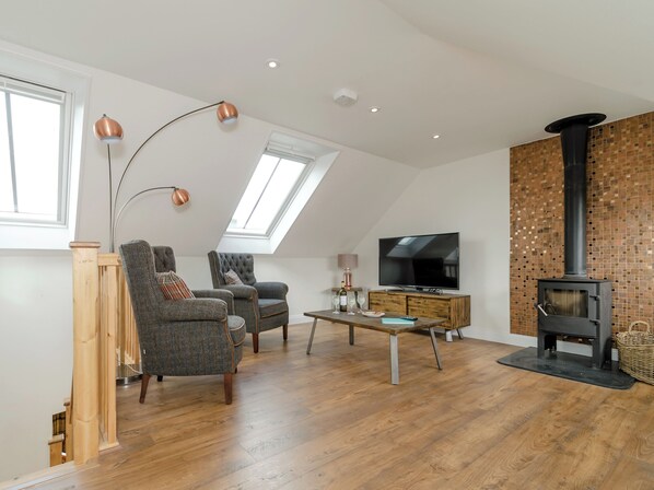 A loft-style living room with a high ceiling, wooden flooring, a fireplace, a television, and two armchairs. - 2 bedroom accommodation in Grinkle, near Staithes (Grinkle, near Staithes)