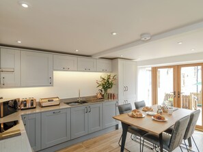 A modern kitchen with grey cabinets, a wooden dining table, and a view of the outside. - 2 bedroom accommodation in Grinkle, near Staithes (Grinkle, near Staithes)