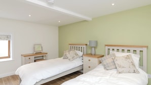 A bedroom with two single beds, a nightstand with a lamp, a small table with a picture frame, and a window with blinds. - 2 bedroom accommodation in Grinkle, near Staithes (Grinkle, near Staithes)