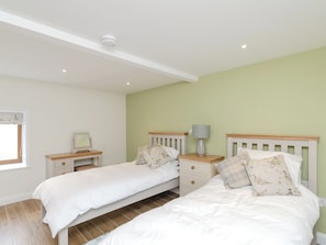 A bedroom with two single beds, a nightstand with a lamp, a small table with a picture frame, and a window with blinds.