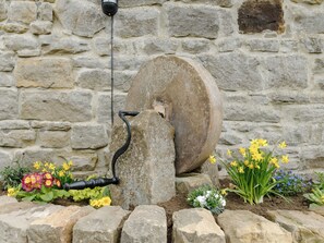A stone wall with a water pump and flower beds.
