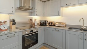 A modern kitchen with white cabinets, a Bosch oven, a stainless steel range hood, a sink, and a countertop with various appliances. - 2 bedroom accommodation in Grinkle, near Staithes (Grinkle, near Staithes)