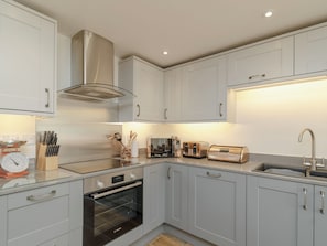 A modern kitchen with white cabinets, a Bosch oven, a stainless steel range hood, a sink, and a countertop with various appliances.