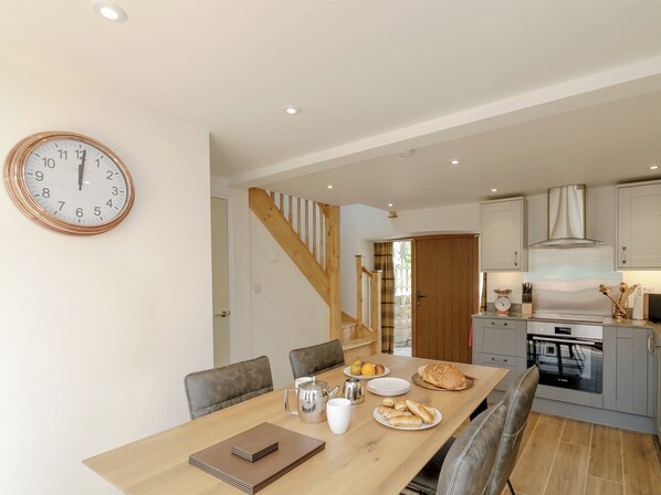 A modern kitchen with a built-in oven, a dining area with a wooden table and chairs, and a staircase leading to another level.