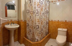 A bathroom with a pedestal sink, toilet, and a shower curtain with a geometric pattern. - Hotel Avenida (Tacna)
