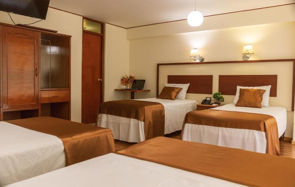A hotel room with two beds, a wooden wardrobe, a bedside table with a lamp, and a television.