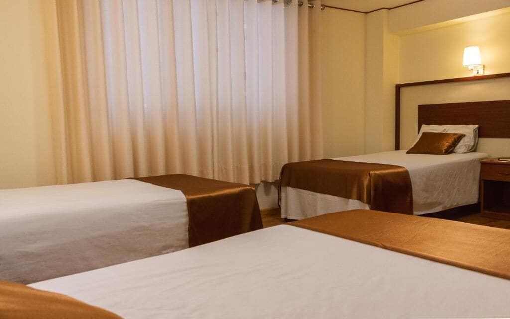 Een hotelkamer met twee eenpersoonsbedden, een nachtkastje en een lamp.