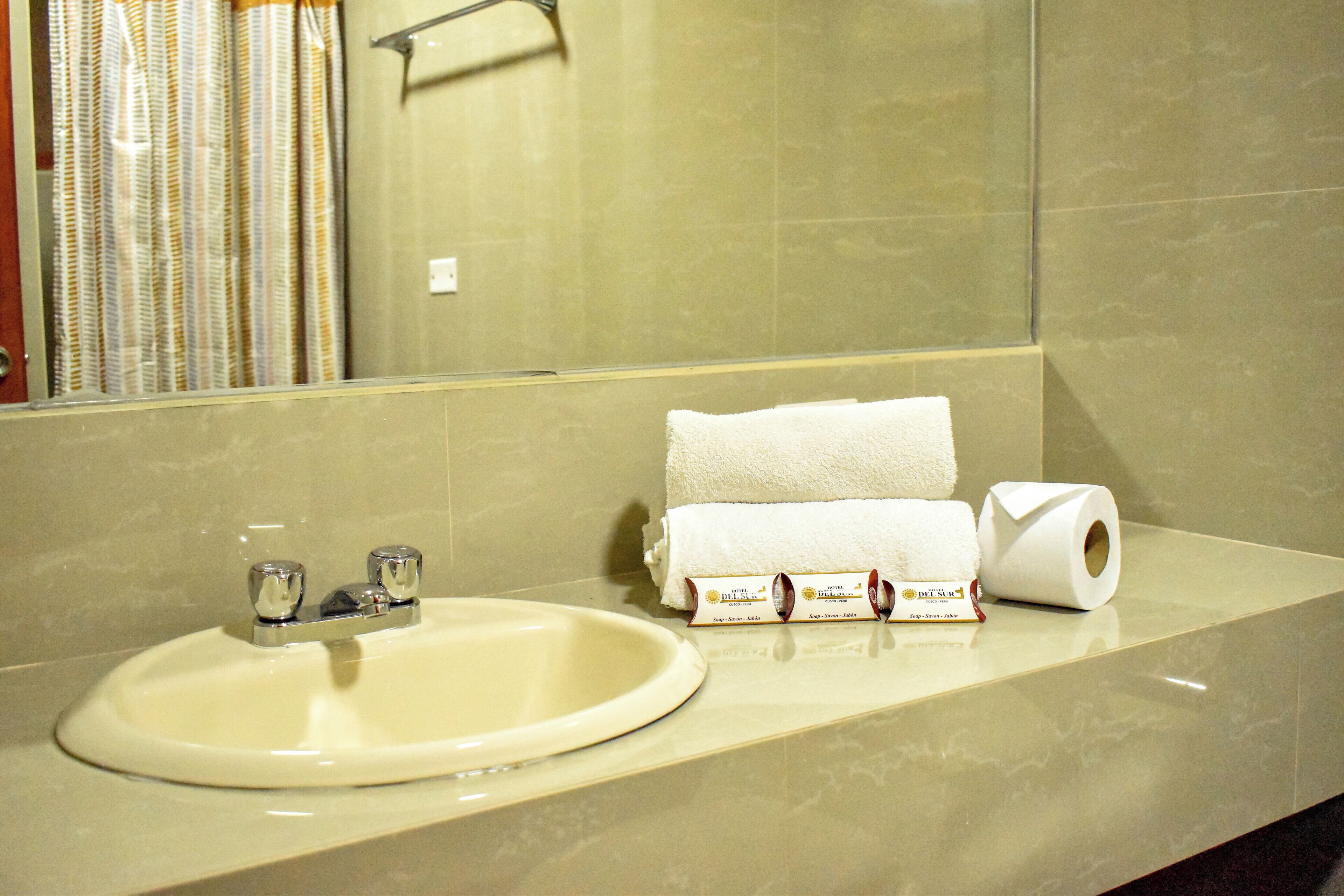 A bathroom with a sink, a mirror, and toiletries including a towel and toilet paper.