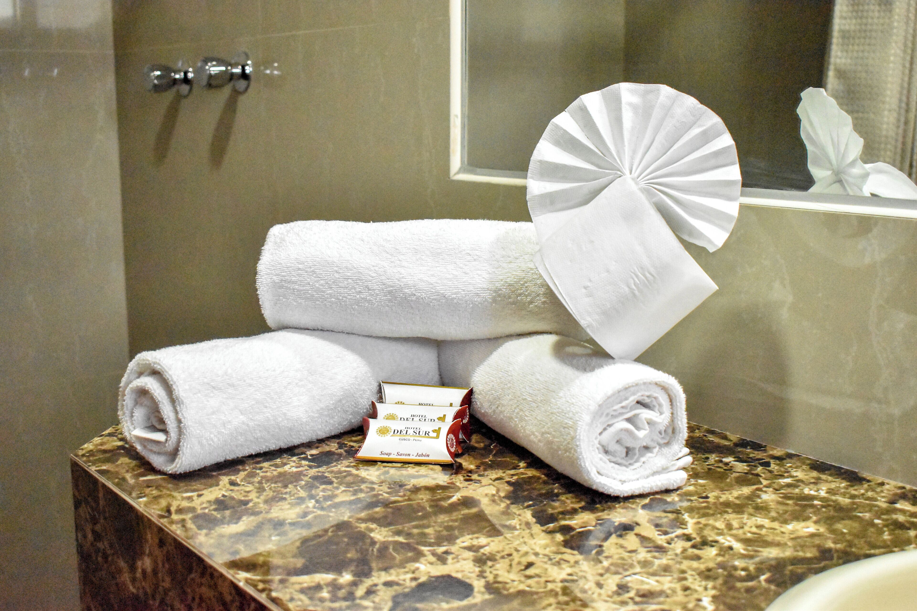 Une salle de bain avec un comptoir en marbre, deux serviettes blanches roulées et un éventail.