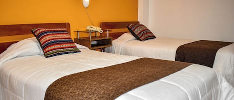Two single beds with white bedding and brown throw blankets, a bedside table with a phone, and a wall-mounted light fixture.