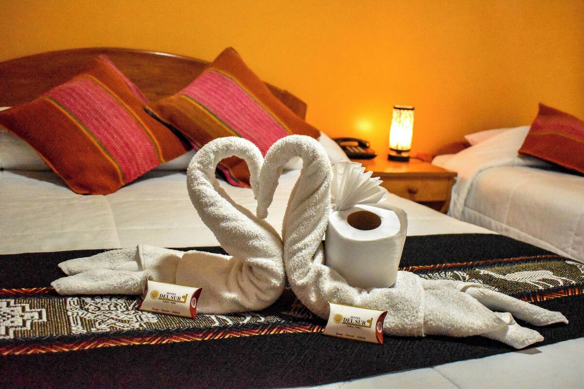 Una habitación de hotel con una cama, almohadas, una lámpara y toallas dispuestas sobre la cama.