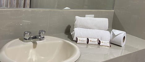 A bathroom with a sink, mirror, towel rack, and toilet paper.