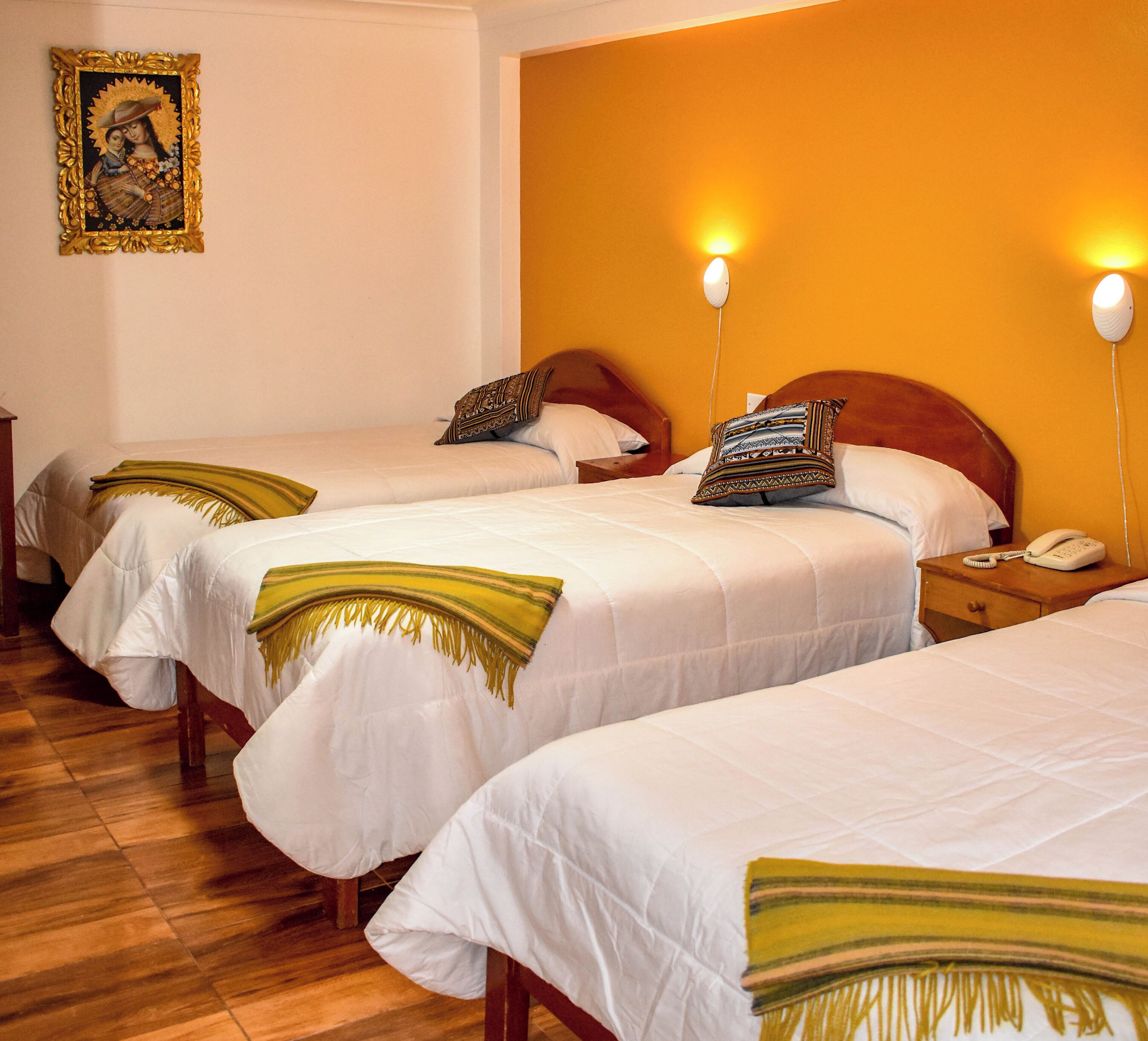 A hotel room with three beds, each with white bedding and a patterned throw. There are two bedside tables with lamps and a telephone.